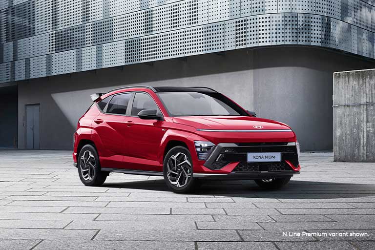 The Hyundai KONA N Line in vibrant red, parked in a modern urban setting, showcasing its bold exterior design, sporty accents, and dynamic stance.